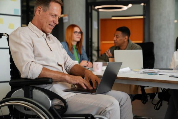Man in a wheelchair working on a laptop in an inclusive office