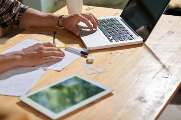 Designer sketching a website plan on paper next to a laptop