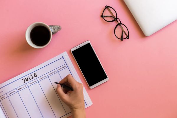 Hand marking appointments on a calendar next to a smartphone