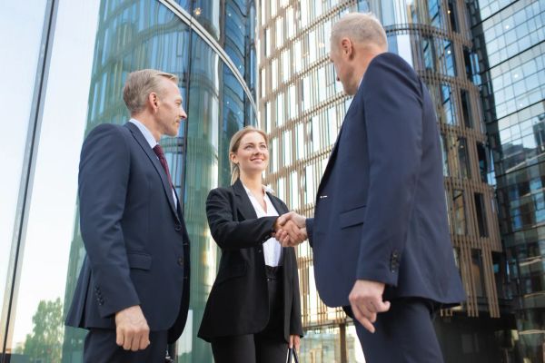 Two business partners shaking hands near an office building