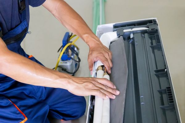 Uniformed HVAC technician repairing an air conditioning unit for a customer