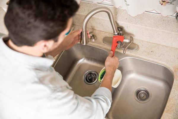 Close-up of a plumber using a wrench to repair a kitchen faucet