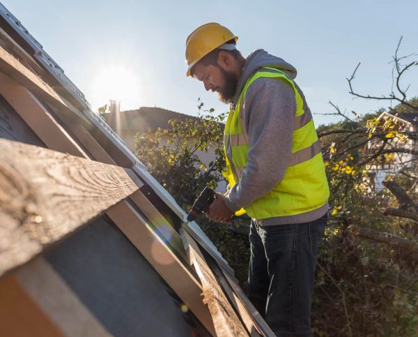 Roofer fastening shingles with a drill