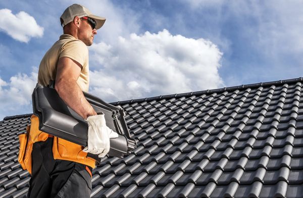 Professional roofer on a finished roof holding roofing materials under a bright blue sky