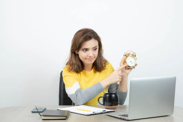 Office worker at her desk pointing at an alarm clock