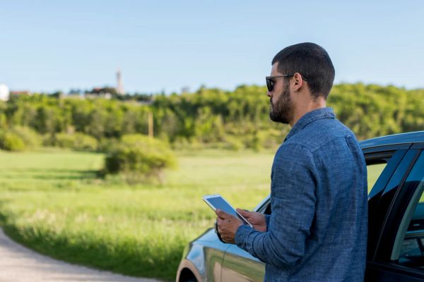 Technician checking a tablet for directions beside his car on a rural road