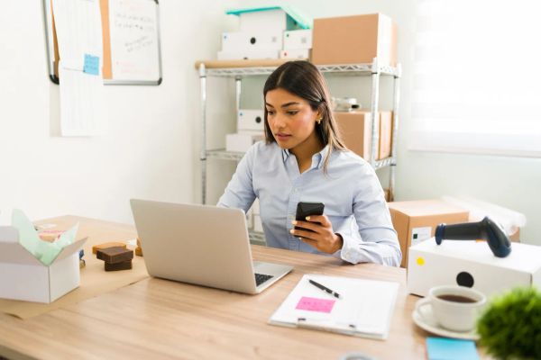 Business owner checking her laptop and smartphone in her office