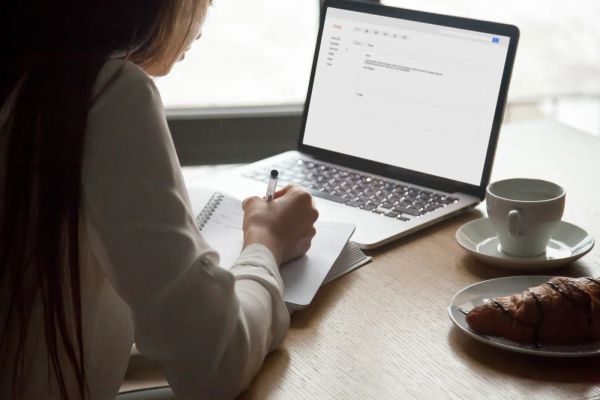Woman at a laptop in a cafe reading and taking notes on an email