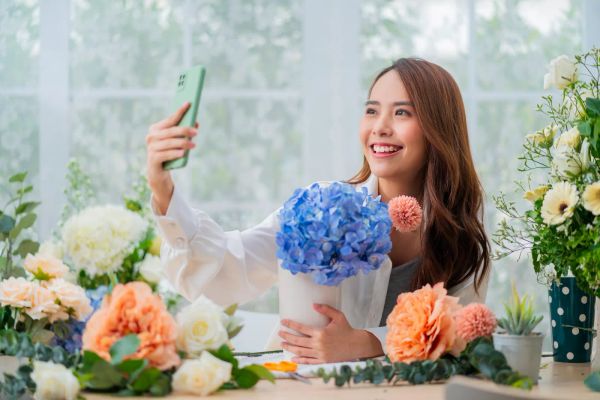 Florist smiling while photographing her flower arrangement for social media