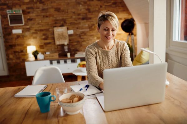 Happy small business owner smiling while using her laptop at home